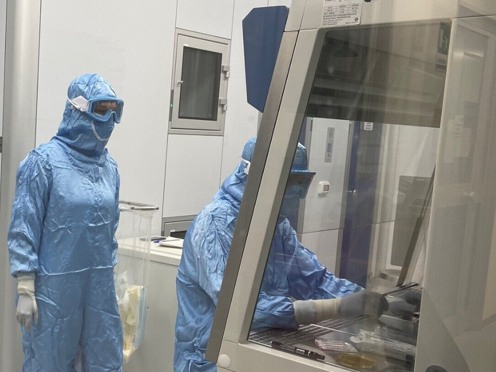 Two researchers in blue cleanroom suits working at a sterile safety cabinet.